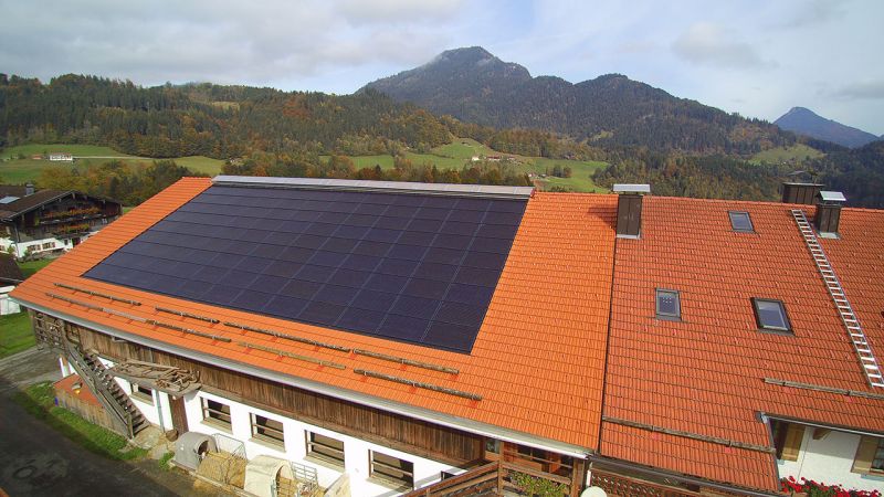 Bergbauernhof in Oberaudorf mit dunklem Solrif-Indachfeld in der roten Ziegeldeckung, Berge im Hintergrund